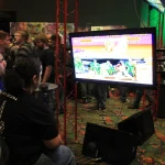 Players sitting together playing video games on a big screen at PAX South 2015